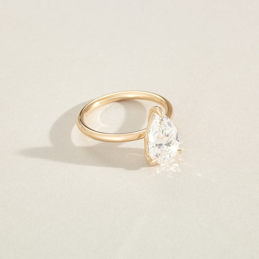 Gold ring with a pear-shaped diamond on a light beige background