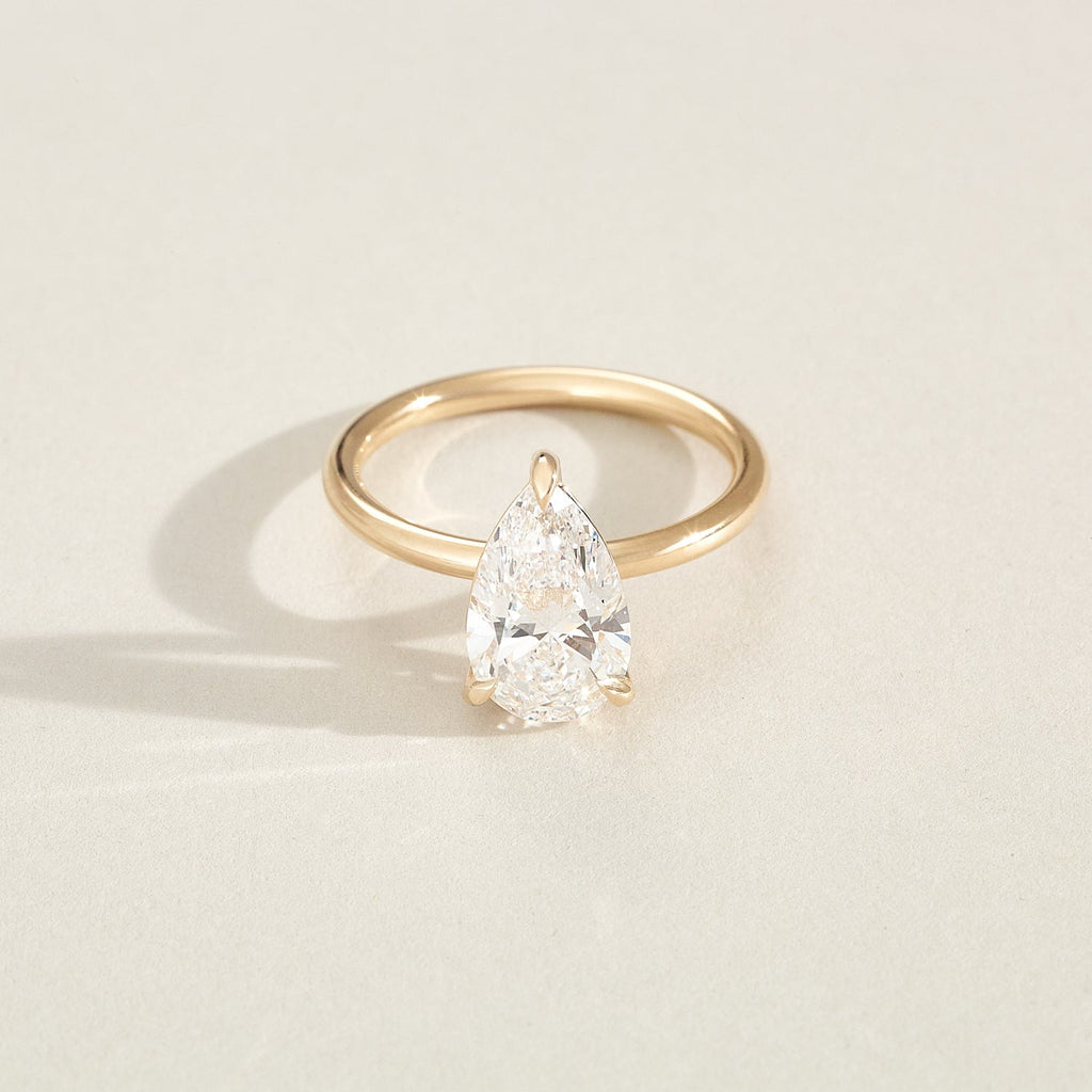 Gold ring with a pear-shaped diamond on a light beige background