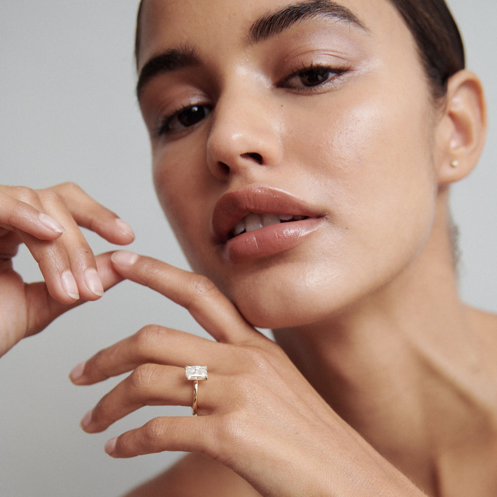 Woman showcasing luxury gold ring with large rectangular gemstone, posing gracefully. Appears polished and sophisticated.[text overlay: Model Wears 2ct Diamond]