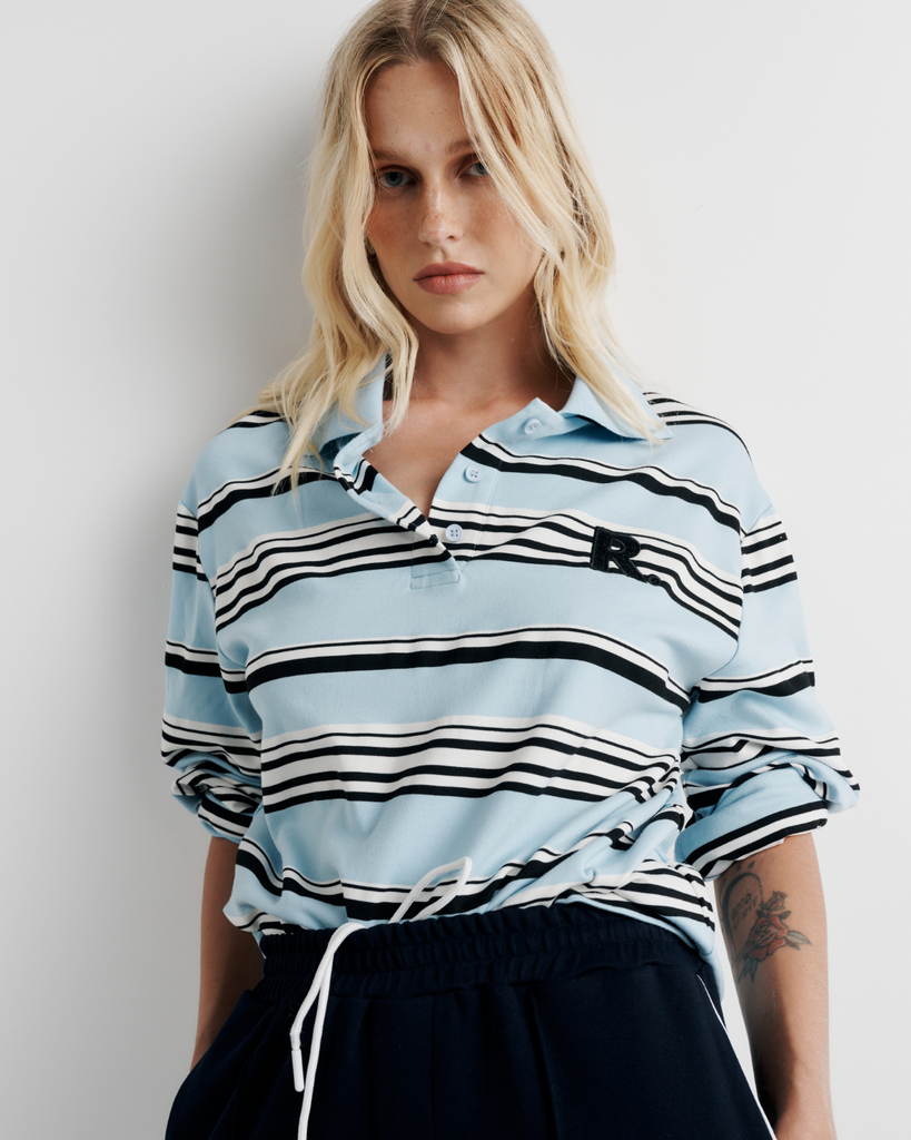 Model wearing the Varsity Polo – blue long sleeve polo shirt with classic collar and relaxed fit by ROMY.