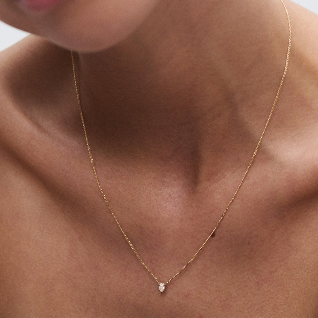 Close-up of a woman wearing a delicate gold necklace with a small teardrop pendant, showcasing luxury jewellery craftsmanship. [text overlay: Pear]