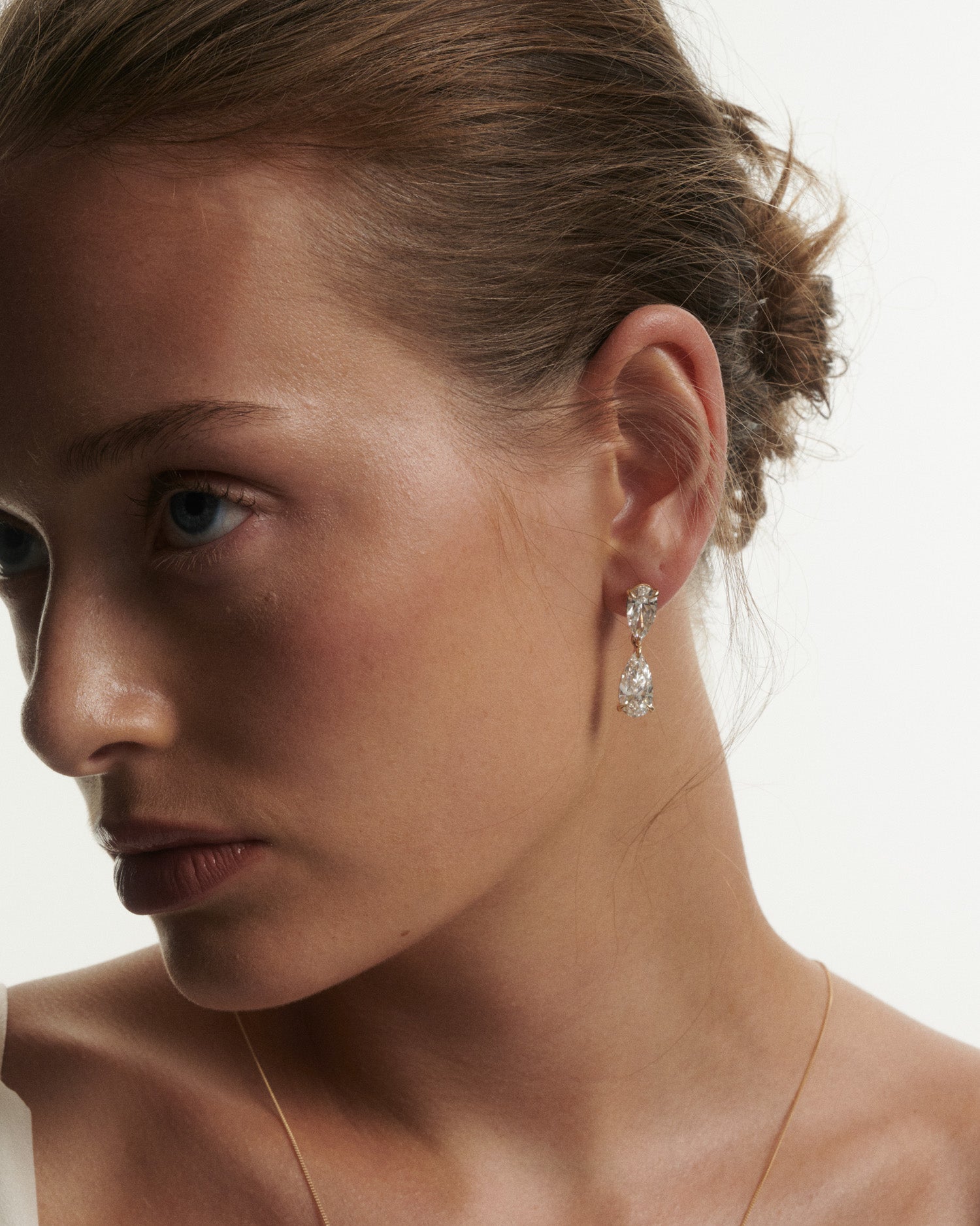 Close-up of a woman wearing diamond earrings with a neutral background