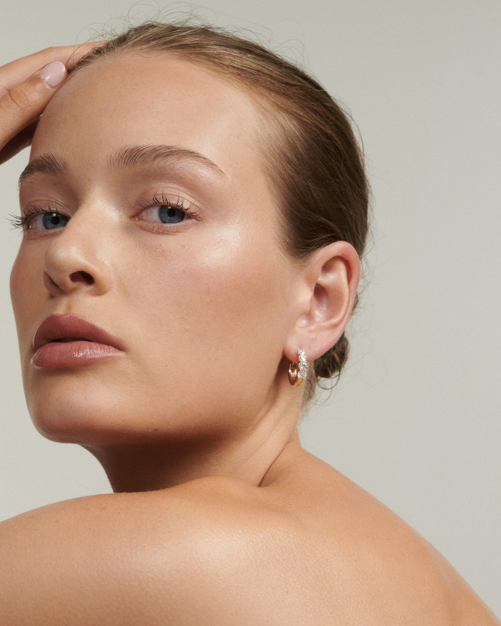 Close-up of a woman's face wearing earrings with a neutral background [text overlay: Bold Diamond Huggies]