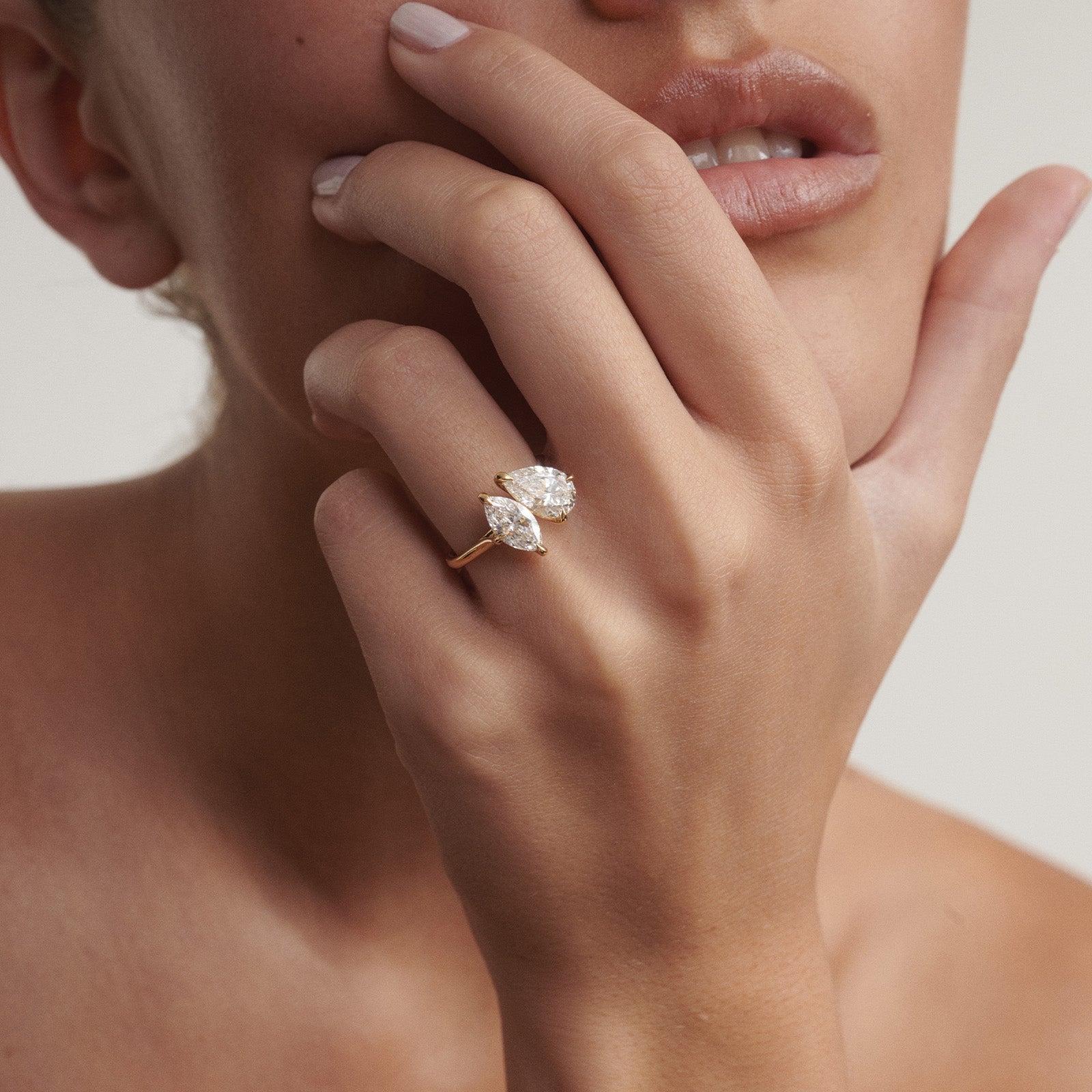 Close-up of a hand wearing a diamond ring on a neutral background