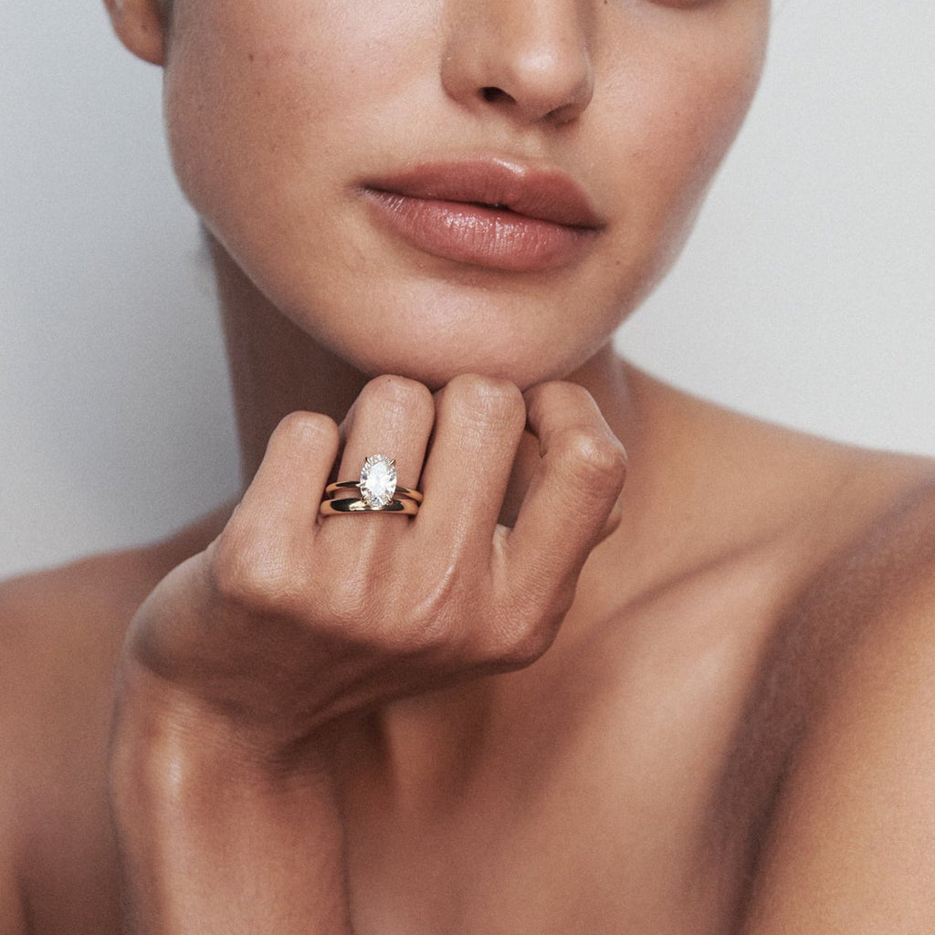 Woman with sleek hair, showcasing a luxurious gold ring with a large pearl, against a soft, neutral background. Elegant jewellery display. [text overlay: 2ct Diamond and Orbit Band]