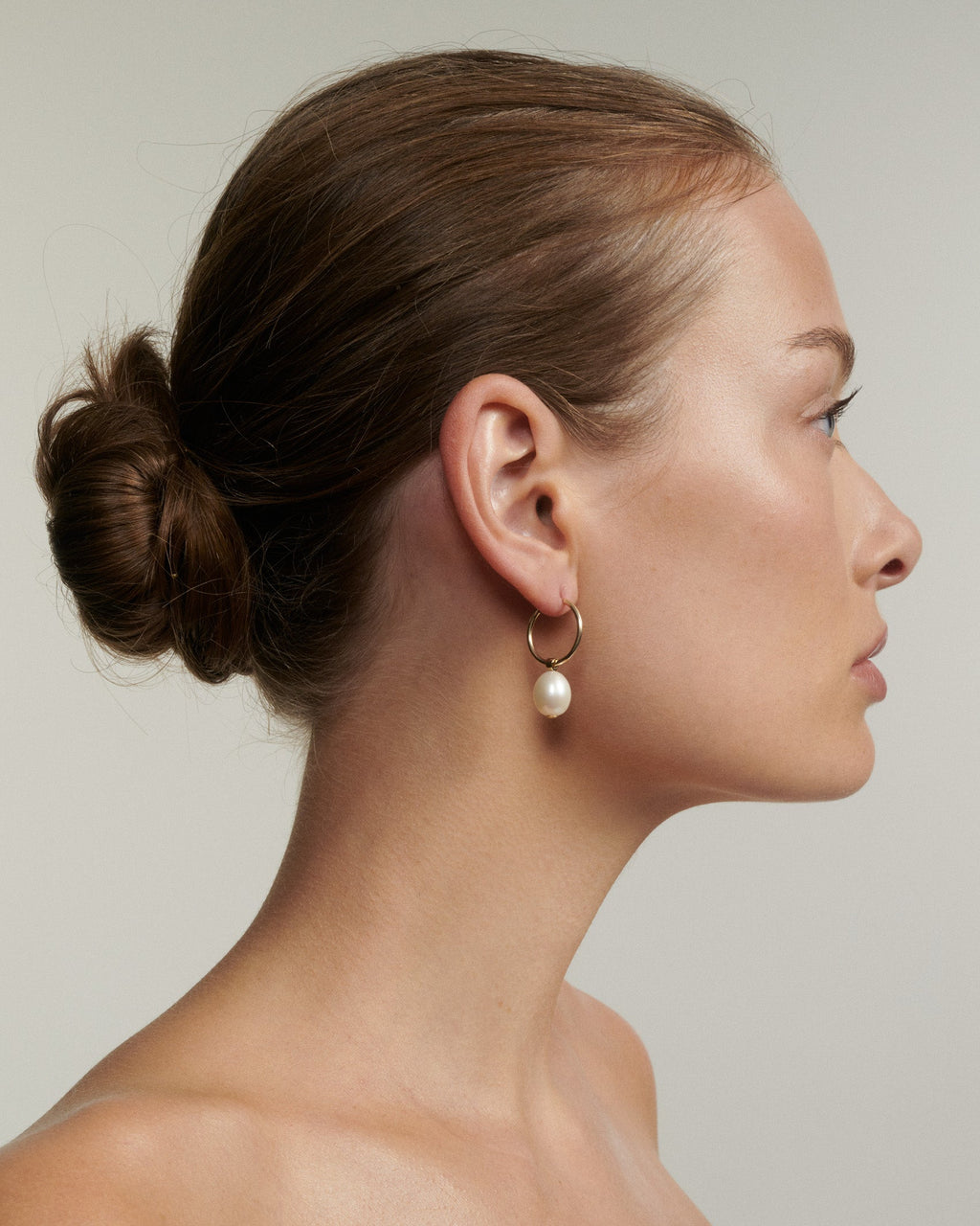 Woman with a side bun wearing a pearl earring against a neutral background