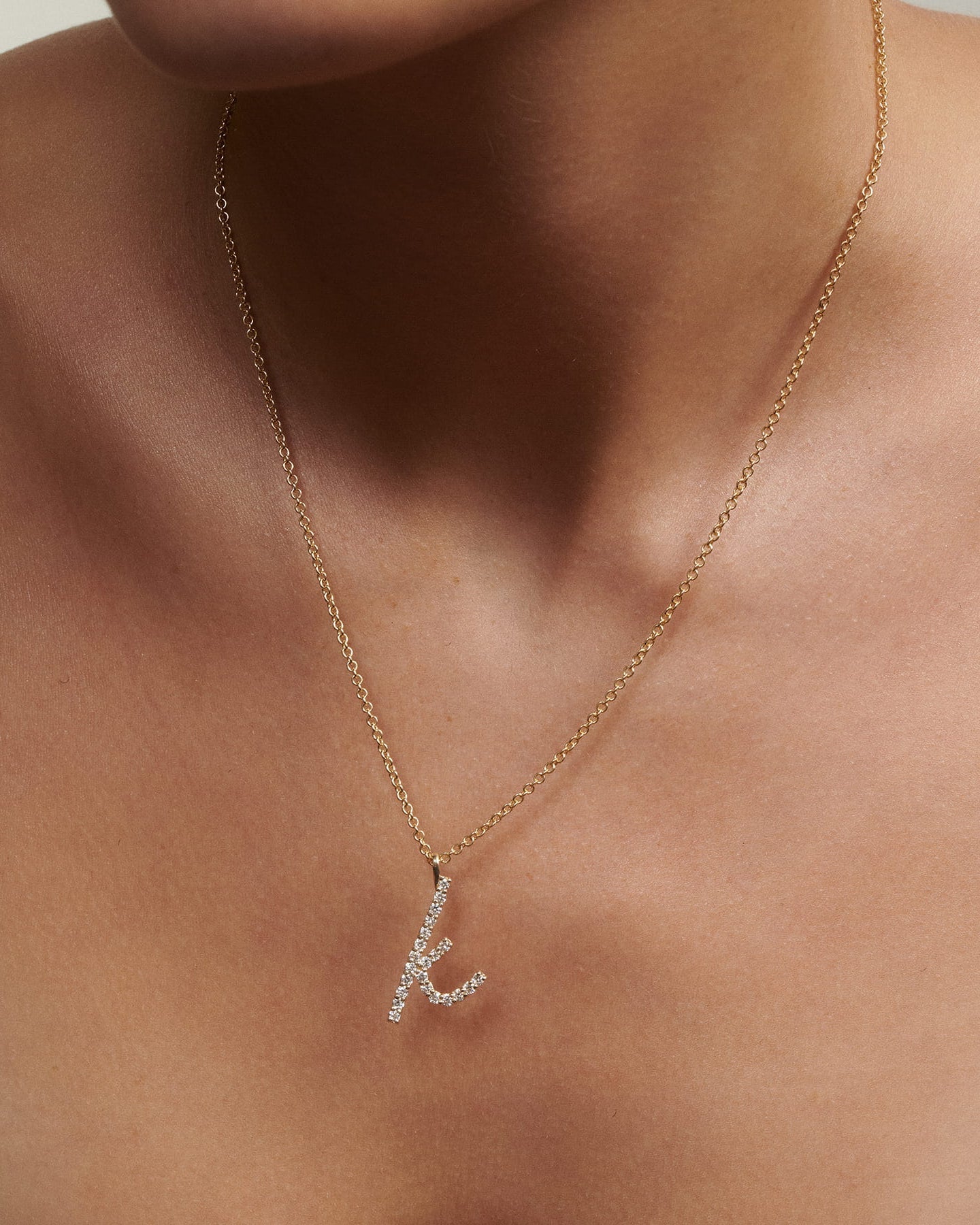 Close up of woman wearing Script Diamond Letter K Necklace in gold