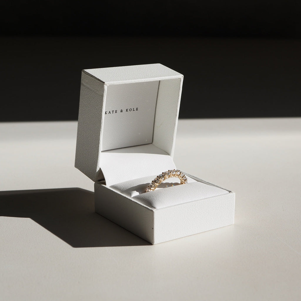 A diamond band sits on a table in a ring box.