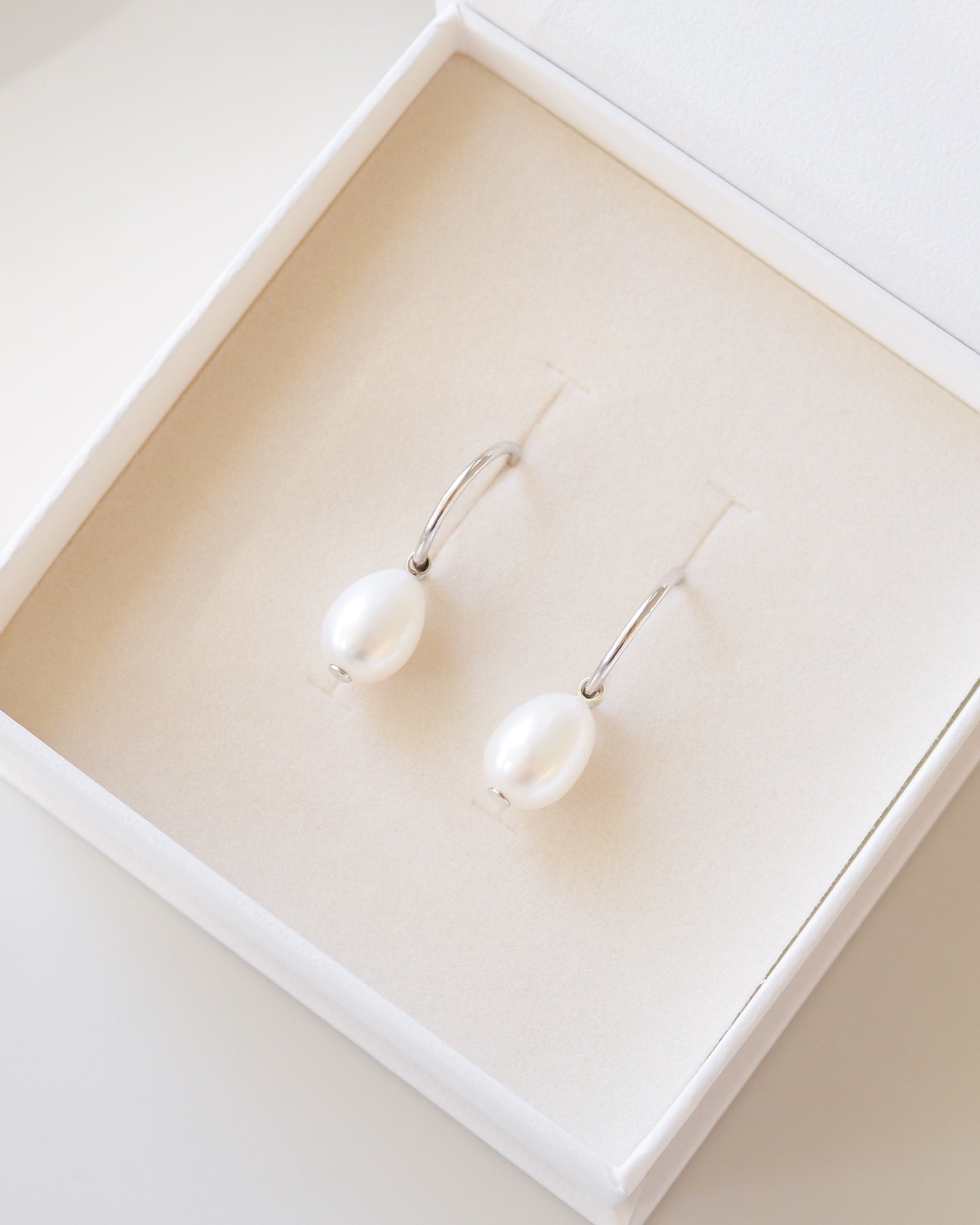 Pearl earrings in a white jewelry box on a light beige background