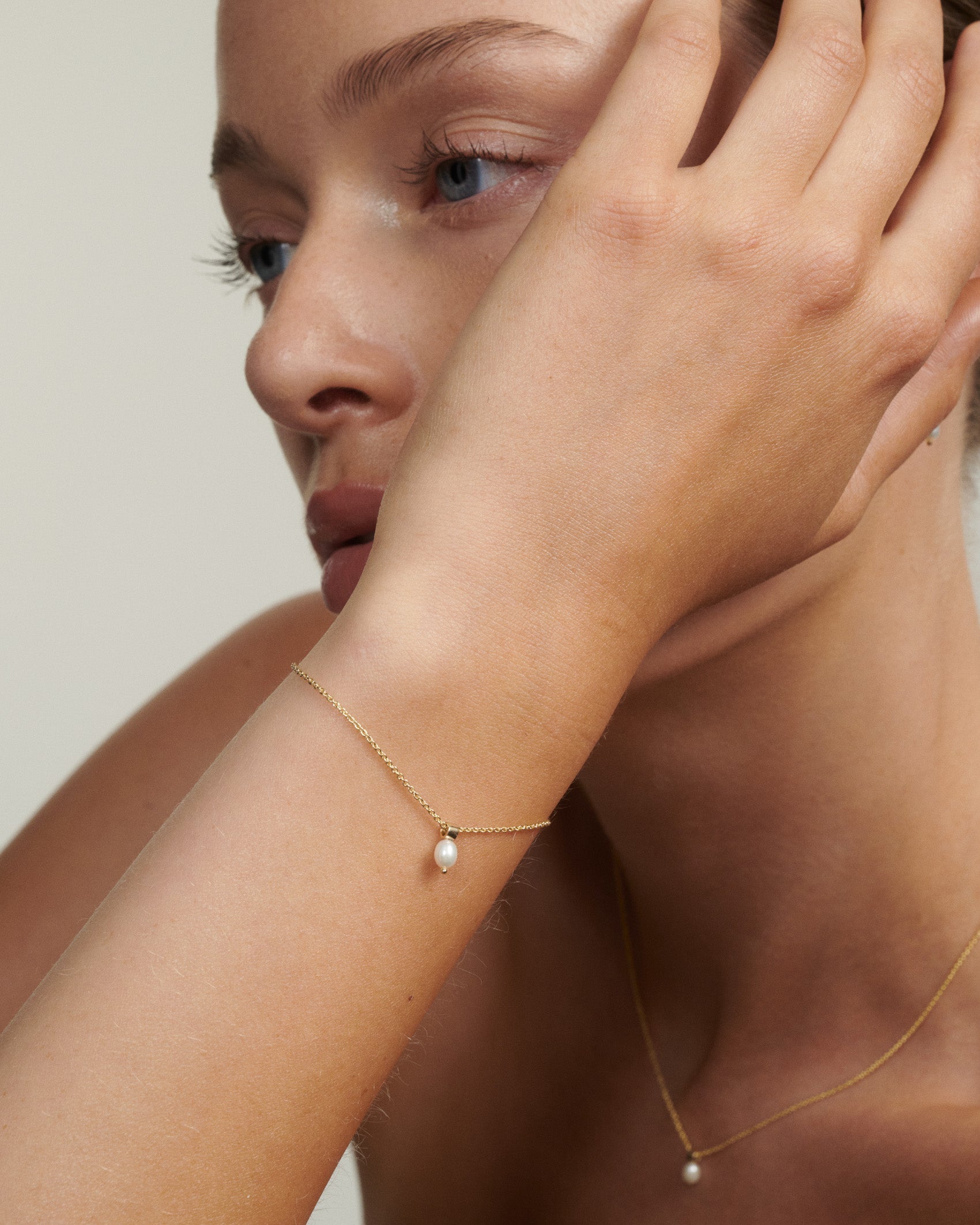 Close-up of a person wearing a delicate gold bracelet and necklace with a pearl pendant.