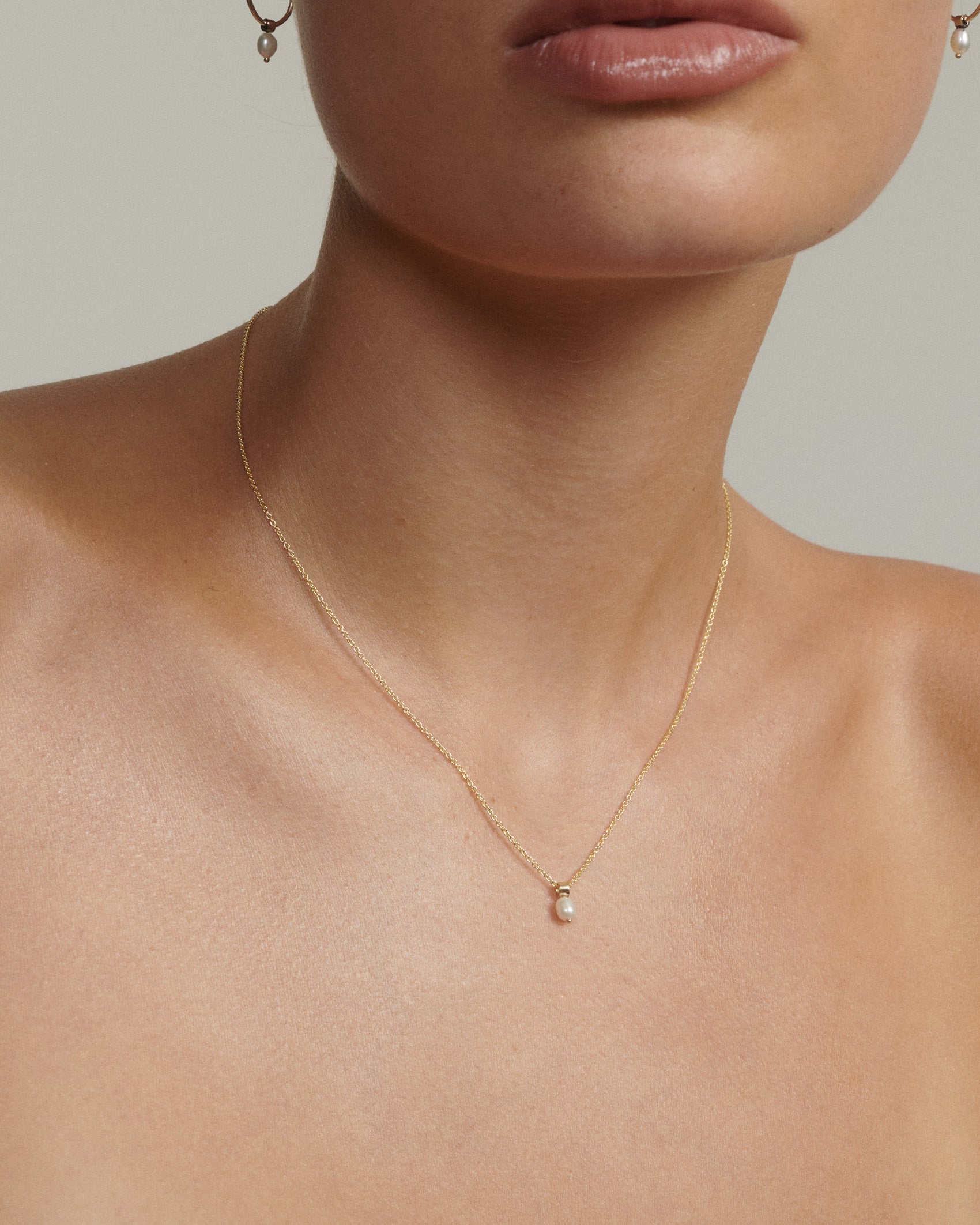 Gold necklace with a pearl pendant on a neutral background
