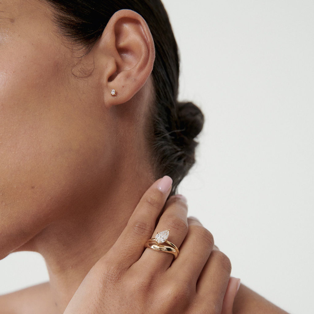 Close-up of a woman wearing elegant gold jewellery: a delicate diamond stud earring and a gold ring with a pear-shaped diamond accent.