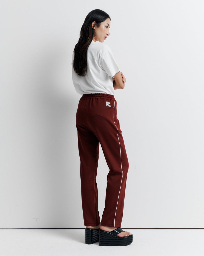 The RAS Track Pant features a comfortable elastic waistband, contrast piping, and pinstitch detailing. Designed with a straight leg, side pockets, internal drawstring, and invisible ankle zips. Finished with the signature Romy Athletic Society 'R' embroidery at the back.