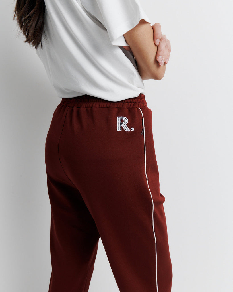 The RAS Track Pant features a comfortable elastic waistband, contrast piping, and pinstitch detailing. Designed with a straight leg, side pockets, internal drawstring, and invisible ankle zips. Finished with the signature Romy Athletic Society 'R' embroidery at the back.
