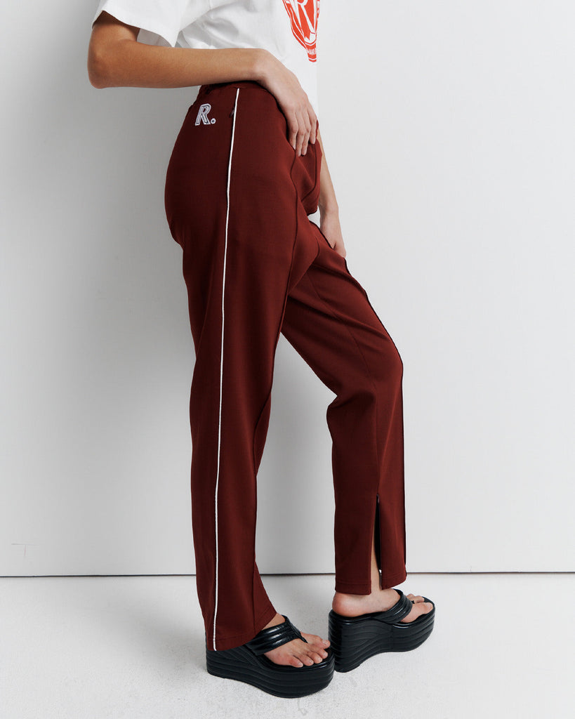 The RAS Track Pant features a comfortable elastic waistband, contrast piping, and pinstitch detailing. Designed with a straight leg, side pockets, internal drawstring, and invisible ankle zips. Finished with the signature Romy Athletic Society 'R' embroidery at the back.