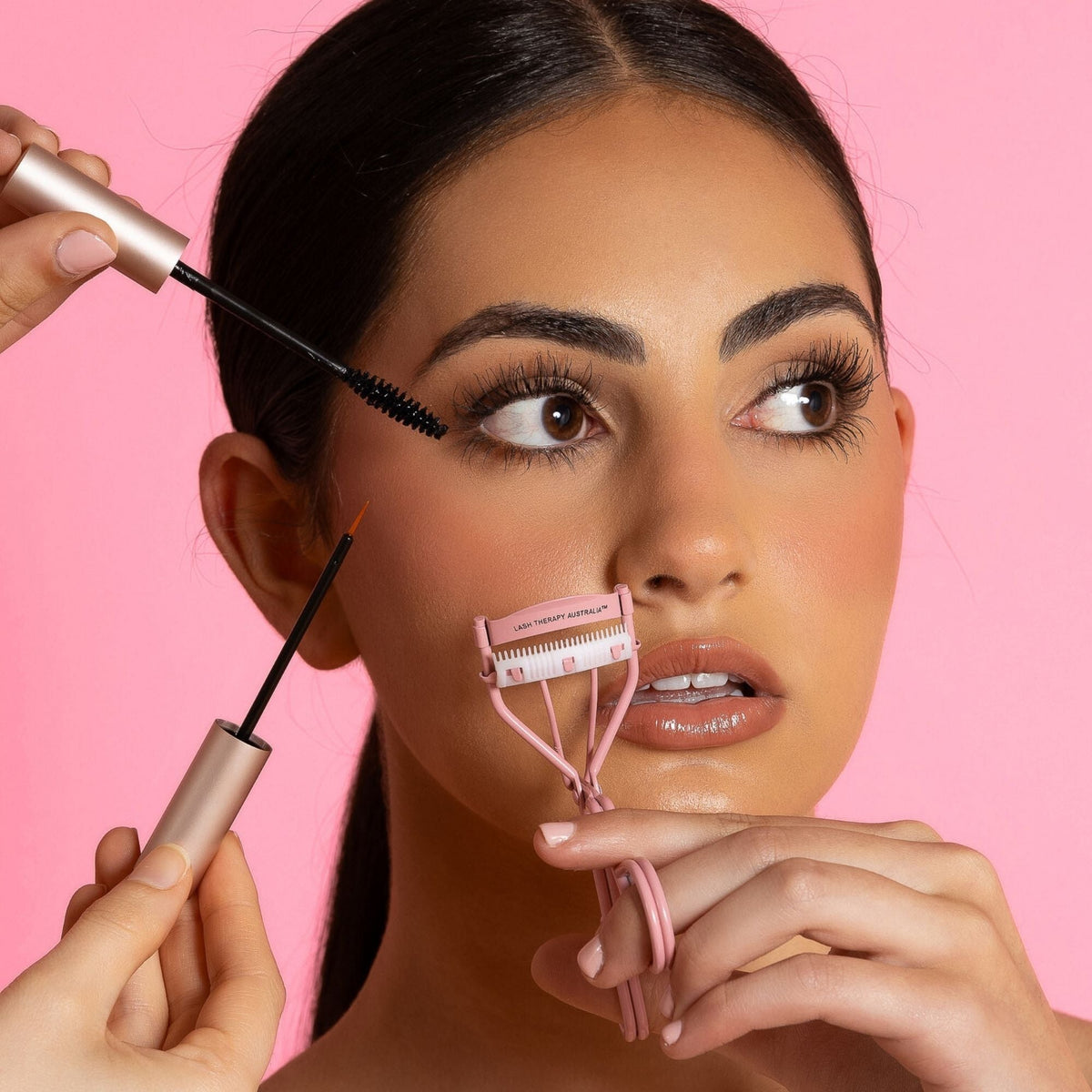 Lash therapy australia model demonstrating Lash Therapy Australia lash routine using eyelash growth serum, growth serum mascara and lash curler on pink background.